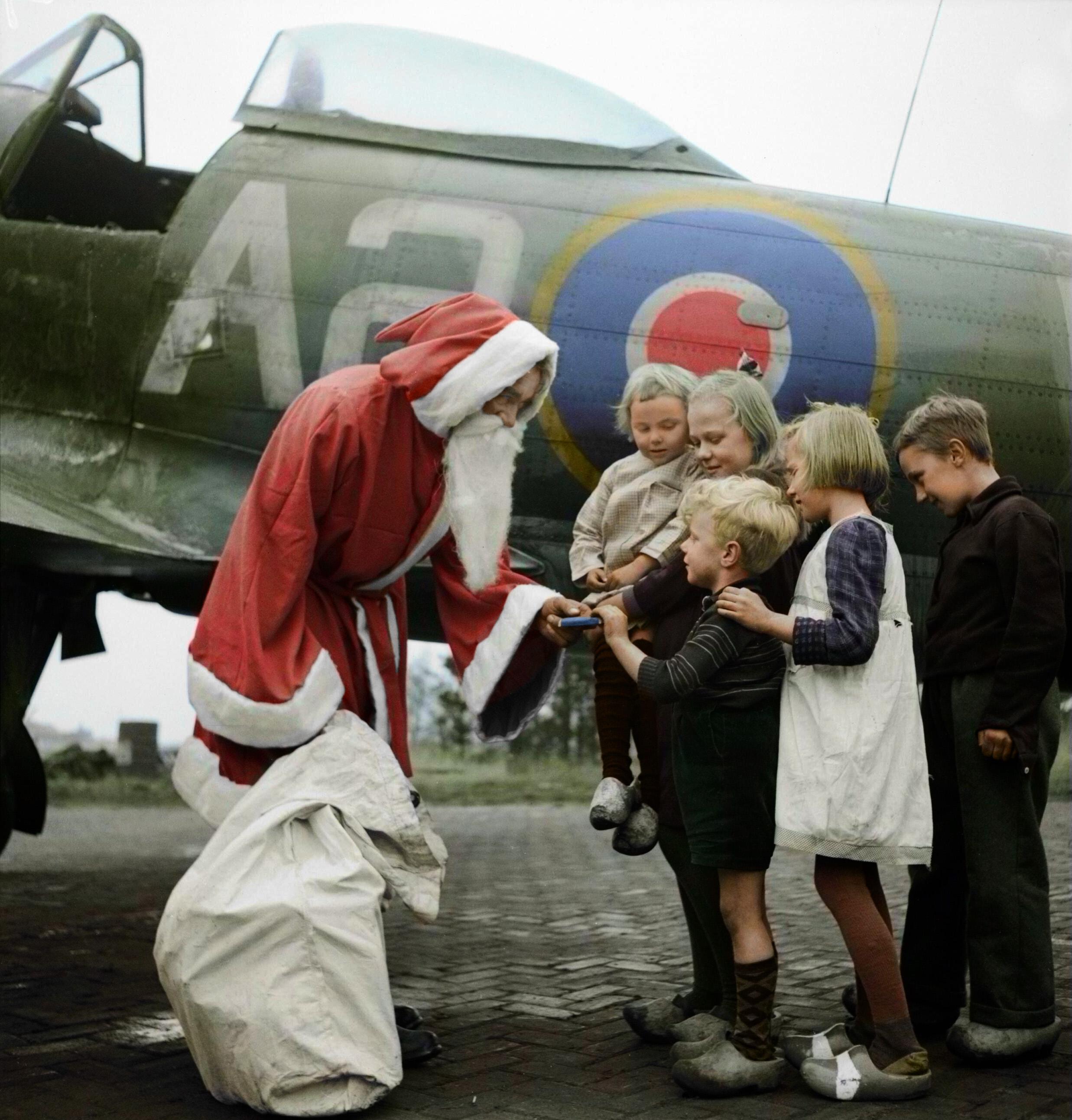 Leading_Aircraftman_Fred_Fazan_dressed_as_Santa_Claus_hands_out_presents_to_Dutch_children_at_No._122_Wing's_airfield_at_Volkel,_Holland,_13_December_1944._CL1729.jpg