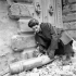 Driver S. Miller of a Canadian reconnaissance regiment examining an artillery shell before its removal, Bagnacavallo, Italy, 3 January 1945.